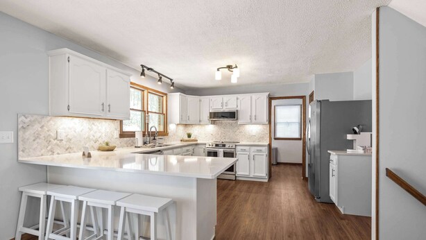 Une cuisine moderne avec des meubles blancs, un grand îlot central doté de tabourets et un plancher en bois.