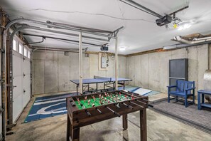 Une pièce avec un baby-foot, deux tables de ping-pong et une chaise bleue.
