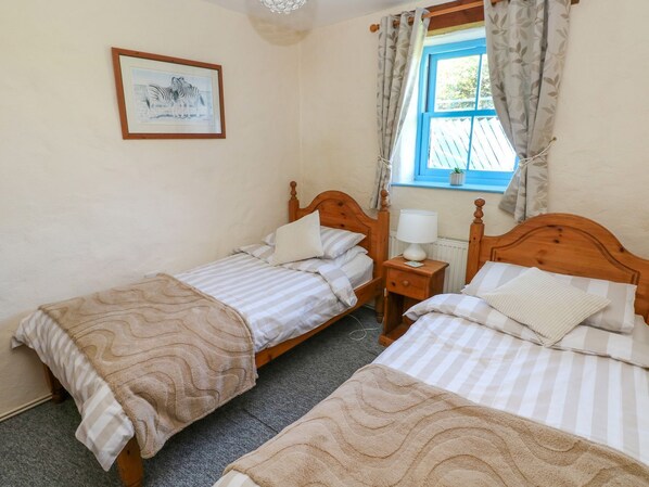 A bedroom with two single beds, a bedside table with a lamp, a framed picture on the wall, and a window with curtains. - Casa Mia (Goodwick)