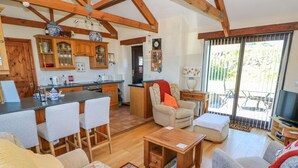 A spacious living area with a kitchen, a dining area, and a seating area with a sofa and chairs. There is a television and a window with a view of the outdoors. - Casa Mia (Goodwick)