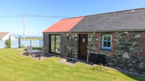 A stone building with a red roof, a door, and a window. There is a lawn and a table with chairs outside. - Casa Mia (Goodwick)