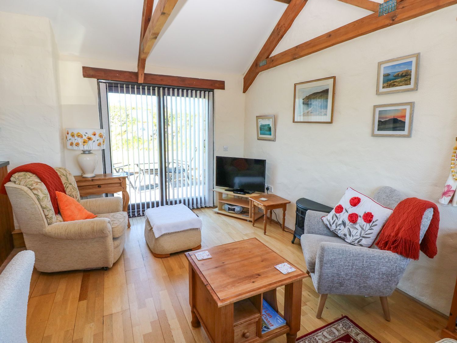 A cozy living room with a wooden floor, a sofa, a chair, a TV, and a balcony with sliding doors.