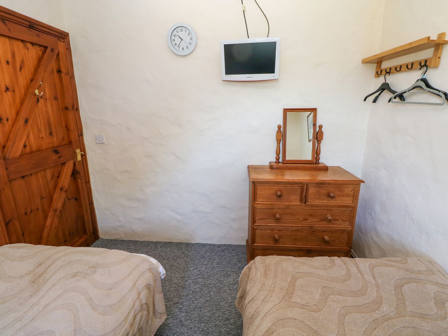 A room with two beds, a wooden dresser, a wall clock, a television, and a coat rack.