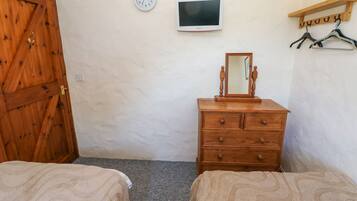A room with two beds, a wooden dresser, a wall clock, a television, and a coat rack.
