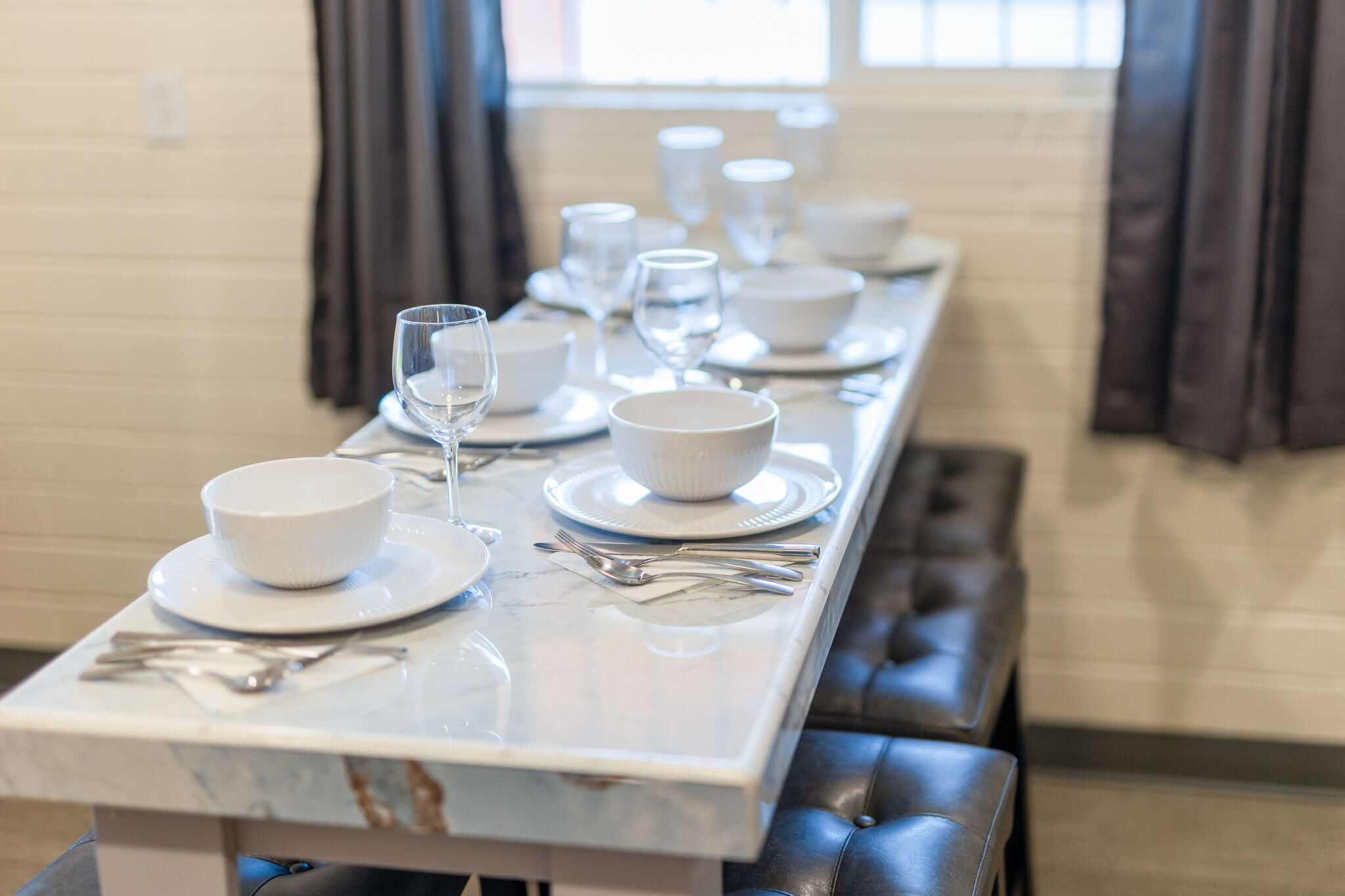 Une table à manger dressée avec de l’assiette, des bols et des couverts blancs, surmontée d’un plateau en marbre et dotée de bancs rembourrés.