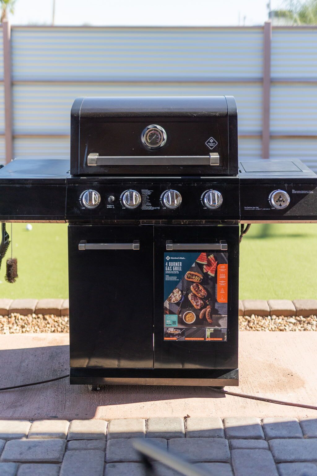A black 4-burner gas grill with a control panel and a promotional booklet.