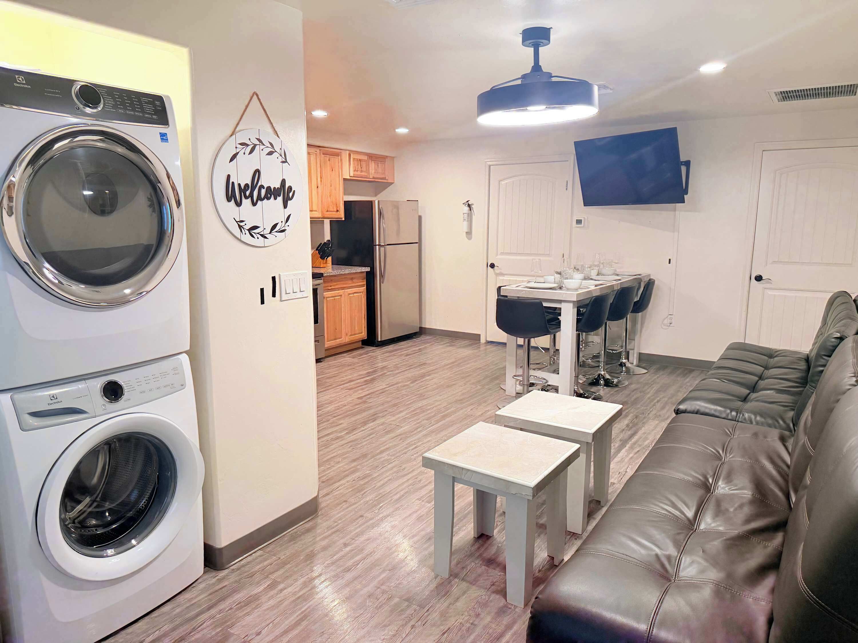 Een modern appartement met een wasmachine, een eethoek met een tafel en stoelen, een bank en een aan de muur bevestigde televisie.