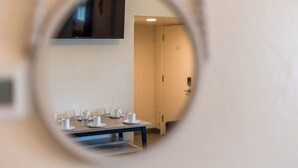 Una habitación con un espejo circular que refleja un comedor con una mesa preparada para cuatro, un televisor montado en la pared y una puerta que da a otra estancia.