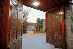 A courtyard with ornate wooden doors, a covered seating area, and a brick wall. - Imperial palace bukhara  (Bukhara)