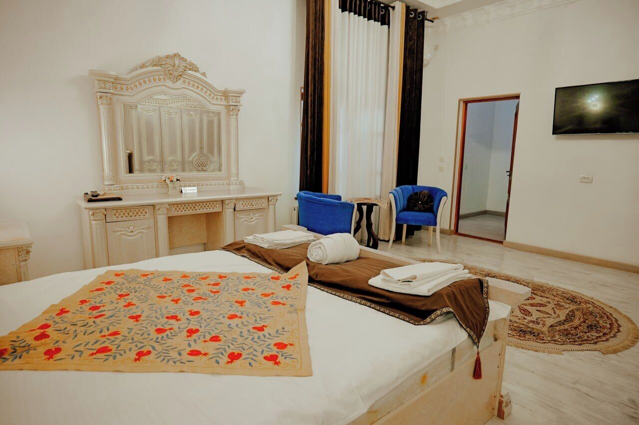 A hotel room with a bed, a vanity with a mirror, a blue chair, and a television on the wall.
