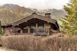 Ein rustikales Holzhaus mit Balkon, umgeben von hohem Gras und Bergen im Hintergrund.