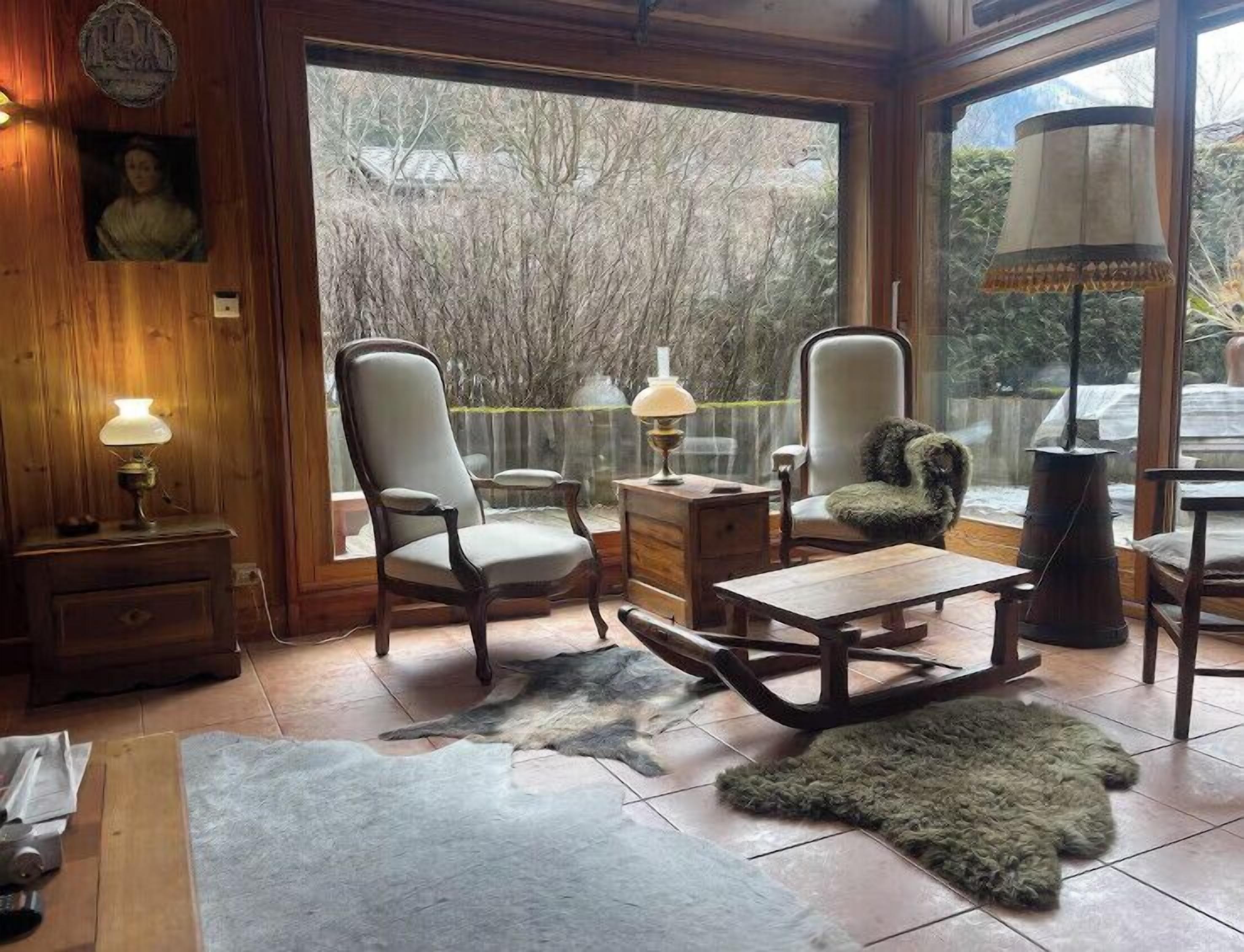 Ein gemütliches Zimmer mit Holzwänden, einem großen Fenster, zwei Stühlen, einem kleinen Tisch und einer Lampe.