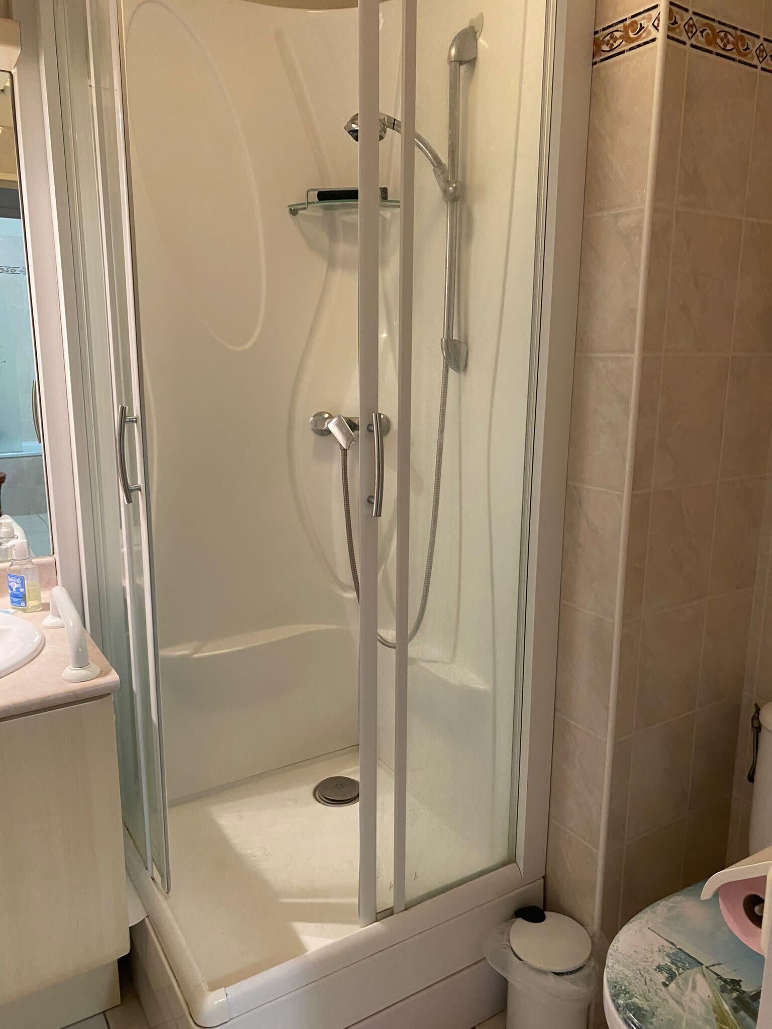Een douchekabinet met glazen wanden, een handdouche en een wandmengkraan.