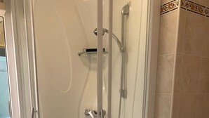 Cabina doccia in vetro con soffione a mano e rubinetto a muro.