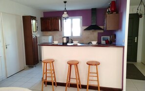 A kitchen with a central island, wooden stools, a refrigerator, a stove, and a window. - House with garden near the sea in Mesquer (Mesquer)