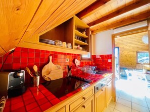 A kitchen with red-tiled backsplash, wooden cabinets, and a black stove. - Ski nest with large balcony (La Salle-les-Alpes)