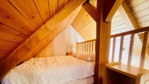 Un dormitorio acogedor en el ático, con techo inclinado de madera, una cama individual, una mesita de noche y un pequeño estante de madera.
