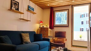 Een kamer met een blauwe bank, een houten plafond, een raam met rood gordijn en een stoel.
