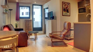 Een moderne woonkamer met een houten plafond, een eettafel, een leren fauteuil en een televisie op een kast.