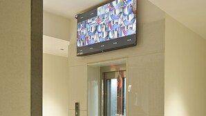 Ein Flur mit einer Panorama-Liftanlage, einem wandmontierten Fernseher, der einen Nachrichtensender zeigt, und einem modernen Innenarchitekturstil.