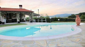 A swimming pool with a stone deck, a covered patio with outdoor furniture, and a view of mountains in the background.