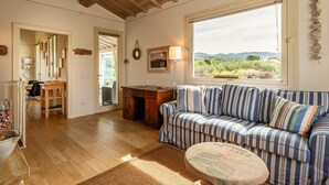 A cozy living room with a striped sofa, a wooden desk, and a large window offering a view of greenery. - Casa Il Cappero – Villa with Private Pool in the Tuscan Hills (San Rocco)