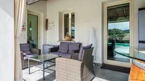 A sunlit patio with wicker furniture, a glass table, and a view of the outdoors. - Casa Il Cappero – Villa with Private Pool in the Tuscan Hills (San Rocco)