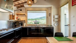 A modern kitchen with a large window, wooden ceiling, and a view of greenery. - Casa Il Cappero – Villa with Private Pool in the Tuscan Hills (San Rocco)