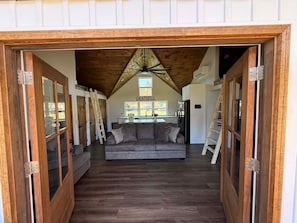 A loft-style room with a wooden ceiling, a gray sofa, and a kitchen area in the background.