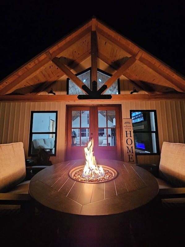 A cozy outdoor seating area with a fire pit, wooden beams, and a welcoming sign.