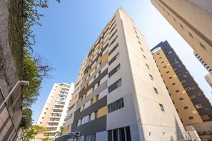 Un edificio residencial alto con varios balcones, fachada plana y cielo despejado.