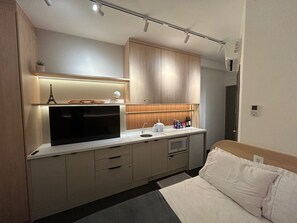 Una habitación de hotel moderna con kitchenette, una cama con ropa blanca y un pequeño modelo decorativo de la Torre Eiffel.