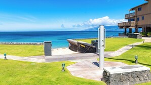 A coastal hotel with a stone pathway leading to a grassy area and a view of the ocean. - Beachfront 2BR Townhouse w/ Ocean Sunset Views (Lahaina)