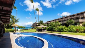 A swimming pool with a circular design, surrounded by a wooden deck and palm trees. - Beachfront 2BR Townhouse w/ Ocean Sunset Views (Lahaina)