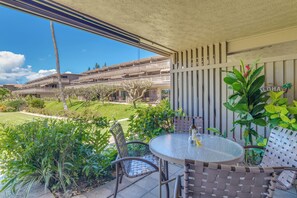 Un espace extérieur aménagé, abrité et doté d’une table et de chaises, offrant une vue sur un immeuble à multiples balcons et un jardin bien entretenu.