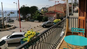 A balcony with a view of a street, parked cars, and a building with a red roof.
