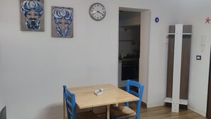 A dining area with a wooden table and blue chairs, a clock, and two paintings on the wall.