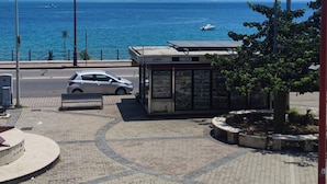 A paved area with a kiosk, a car, and a view of the sea and mountains.