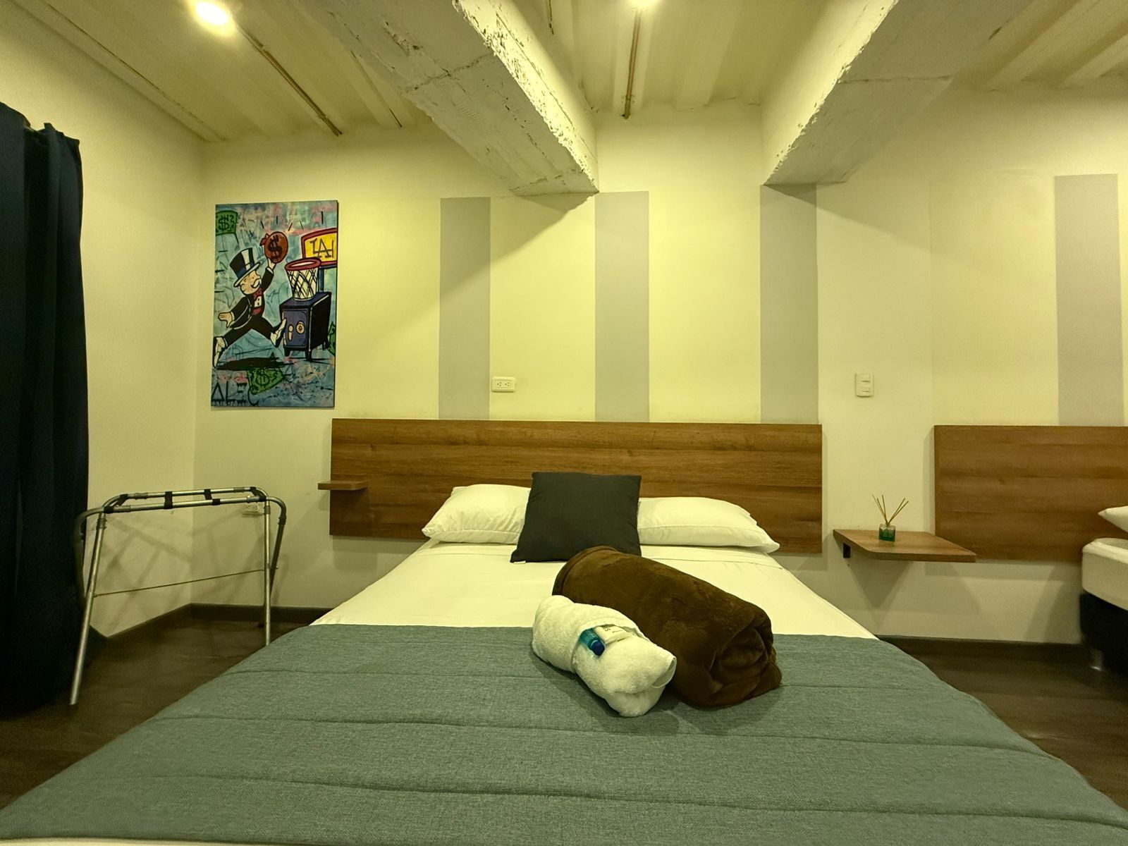 A hotel room with a large bed, a wooden headboard, a painting on the wall, and a small bedside table with a candle.