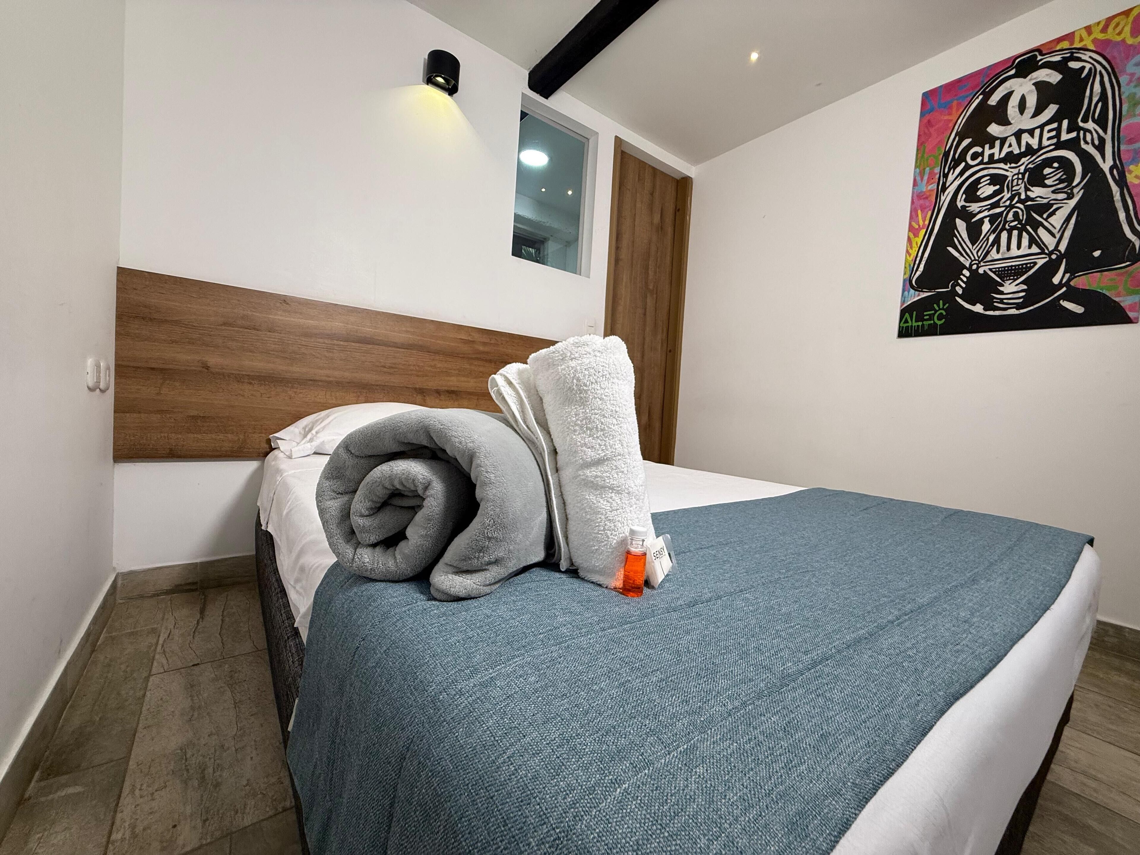 A neatly made bed with a blue bedspread, a rolled gray blanket, and a white towel.