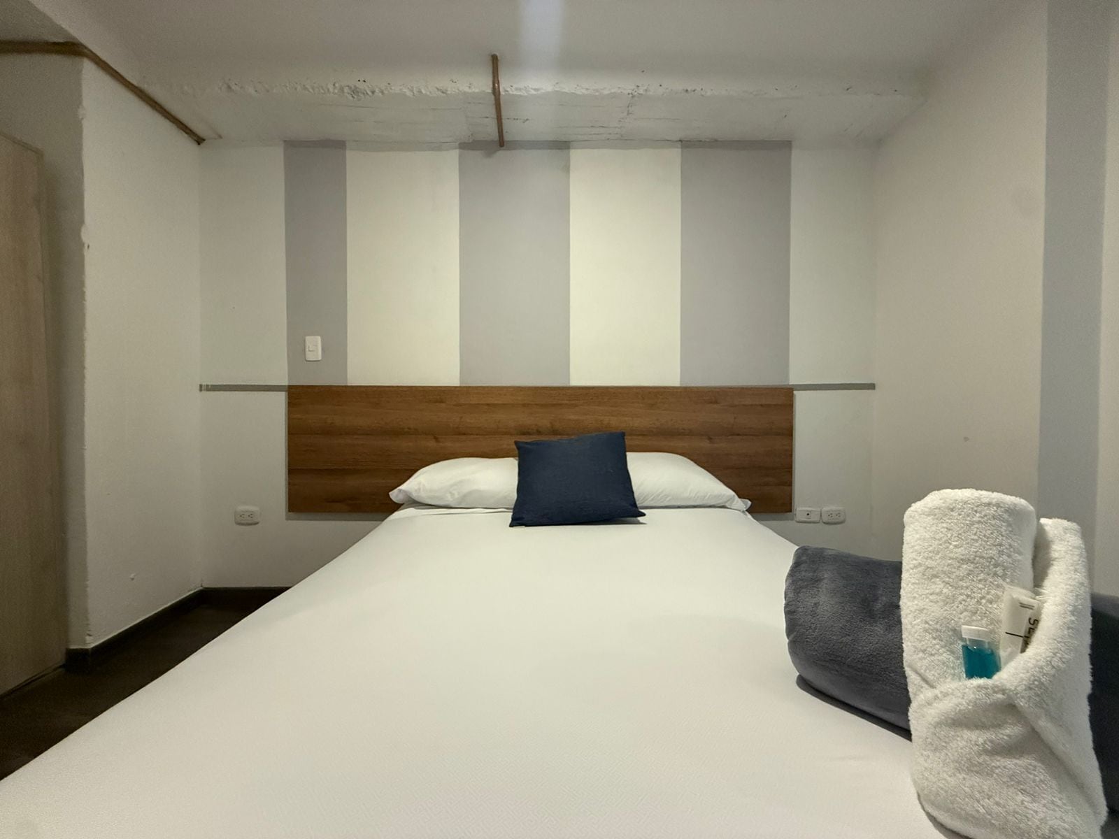 A single bed with a wooden headboard, white bedding, and a blue pillow. A white towel is draped over the bed.