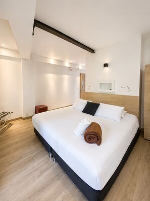 A modern hotel room with a large bed, a wooden headboard, a small bedside table, and a wall-mounted shelf. - Carriqui Underground  (Pereira)