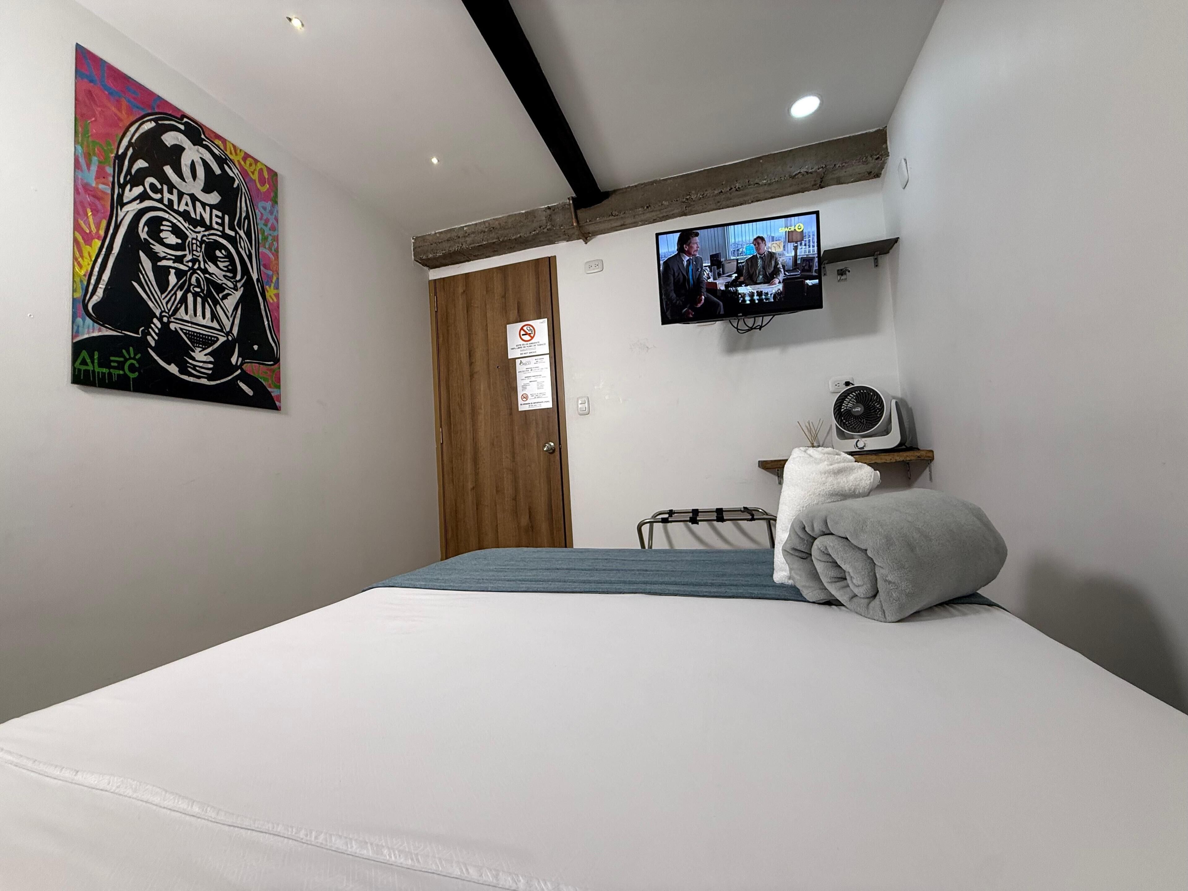 Ein Hotelzimmer mit Bett, Wandfernseher, Holztür und einem Poster an der Wand.