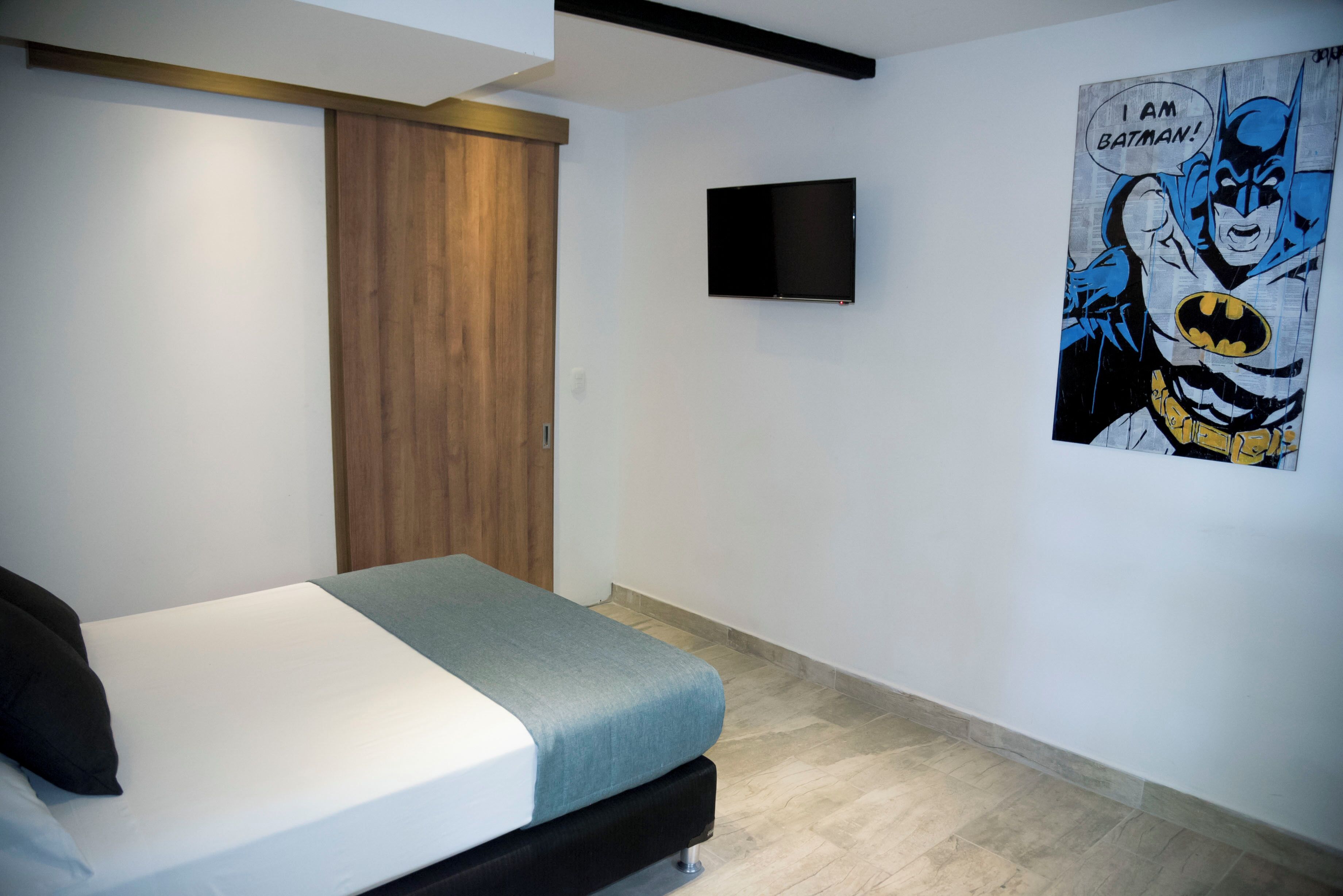 Ein Schlafzimmer mit einem Bett, einem Holzschrank, einem Flachbildfernseher und einem Batman-Poster an der Wand.