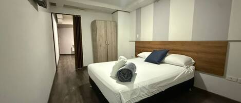 Habitación de hotel con una cama, cabecera de madera, armario y televisor montado en la pared.