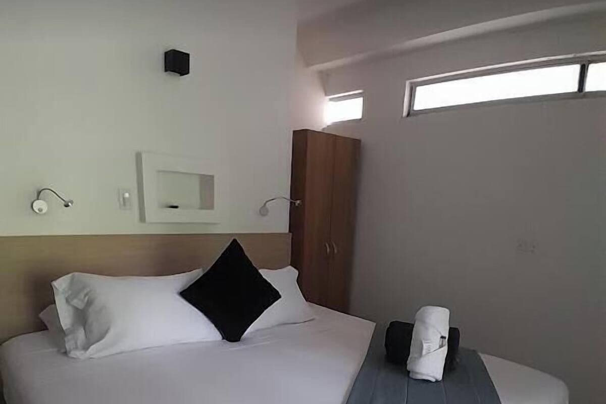 Habitación de hotel con cama, armario de madera, una ventana pequeña e iluminación empotrada en la pared.