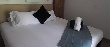 A hotel room with a bed, a wooden wardrobe, a small window, and a wall-mounted light fixture.