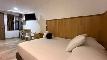 Een hotelkamer met een groot bed, een bureau, een stoel en een aan de muur bevestigde televisie.