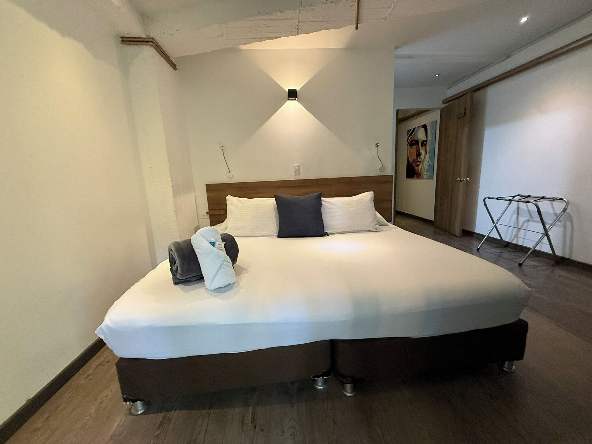 A large bed with a wooden headboard, a bedside table, and a wall-mounted light fixture.