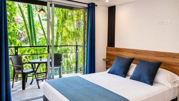 A hotel room with a bed, a balcony with a table and chairs, and a view of greenery. - Carriqui Underground  (Pereira)